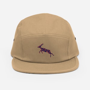 Könnte beinhalten: Eine beigefarbene 5-Panel-Kappe mit schwarzem Schirm und einem gestickten Antilopen-Motiv in Blau und Rot auf der Vorderseite.