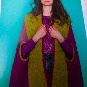 May include: A green and purple knitted cardigan with a shawl collar. The cardigan is open in the front and the model is wearing it over a lace top.