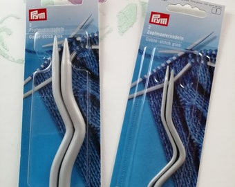 Puede incluir: Dos juegos de agujas de tejer circulares grises en un paquete de plástico. Las agujas miden 6,0 mm/8,0 mm y 4,0 mm. El paquete incluye el texto "Zopfmusternadein Cable-stitch pins" y "Aiguilles pour torsade".