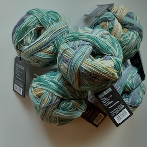 May include: Five balls of yarn in shades of green, blue, and beige. The yarn is a variegated blend with stripes of color. The yarn is packaged in black labels with white text. The label reads "100g Baumwolle Mix, Farbe 013,  Fadenstärke 4,  Made in Germany".