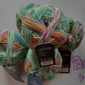 May include: Three balls of colorful yarn in shades of green, pink, yellow, and blue. The yarn is wrapped in a ball shape and has a tag attached to it that says "100g".
