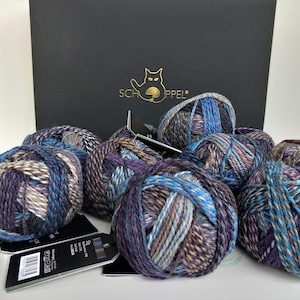 May include: Six balls of yarn in shades of purple, blue, brown, and white. The yarn is arranged in a circle on a white surface. The yarn is labelled "Schoppel".