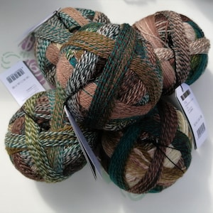 May include: Four balls of yarn in shades of brown, green, and white. The yarn is arranged in a pile, with the labels facing outward. The labels have text in a foreign language.