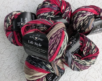 Puede incluir: Varias madejas de hilo multicolor, principalmente rojo, negro, crema y marrón. Cada madeja tiene una etiqueta con el texto "Life Style" y la marca "SCHOPPEL". El hilo es una mezcla de tonos, dando un aspecto texturizado.