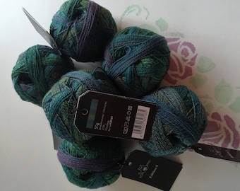 Puede incluir: Cinco ovillos de lana en tonos de verde, azul y morado. La lana está envuelta en espiral. La lana está etiquetada con "50g" y "100% Merino Superwash 100m 110 yds".
