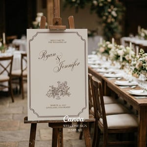 May include: A rectangular wedding welcome sign on a wooden easel with a cream background and dark brown border. The text reads: Welcome to the wedding of Ryan & Jennifer, March 10, 2057, Loveland, Colorado, with a floral line art illustration.