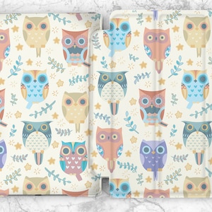 Puede incluir: Una funda blanca para iPad con un patrón repetitivo de búhos coloridos, estrellas y hojas. Los búhos son de varios colores, incluyendo azul, rosa, amarillo y morado.
