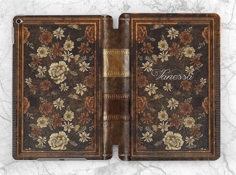 Pu&ograve; includere: Una custodia per iPad con un design a libro vintage. La custodia presenta una texture simile alla pelle marrone scuro con motivi floreali nei toni del marrone e del crema. Il nome "Vanessa" &egrave; scritto sulla copertina.