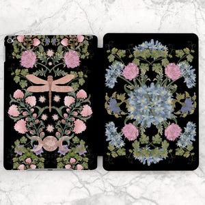 Puede incluir: Una funda negra para tableta con un diseño floral. El diseño incluye flores rosas y azules, hojas verdes y una libélula. La funda está abierta, revelando el interior. El patrón es simétrico y detallado.