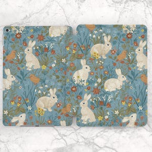 Puede incluir: Una funda de teléfono azul y blanca con un patrón floral y conejos blancos. Los conejos están rodeados de flores, hojas y pájaros.