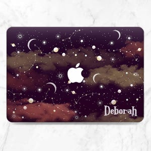 May include: A laptop case featuring a celestial design with constellations, planets, and crescent moons against a dark purple and red cloudy background. The Apple logo is prominently displayed, with the name "Deborah" in white script.