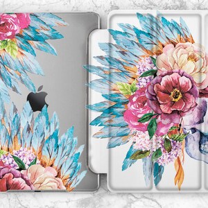 May include: A white case for an iPad with a watercolor design of a skull wearing a headdress of blue feathers and pink, white, and purple flowers.