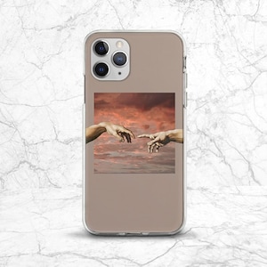 May include: A clear phone case with a brown background and a picture of two hands reaching towards each other against a sunset sky.