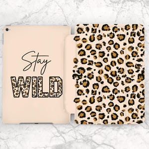 Puede incluir: Una funda de tableta de color beige claro con estampado de leopardo. La funda está abierta, revelando la tableta en el interior. El texto "Stay WILD" está impreso en la funda de la tableta. La palabra "WILD" tiene un estampado de leopardo.