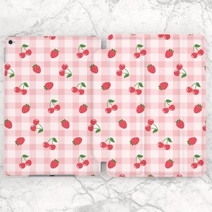 May include: A pink and white gingham pattern tablet case featuring a repeating pattern of red strawberries and cherries with green stems. The case is open, revealing the interior and exterior design.
