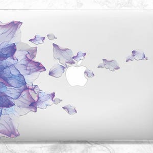 May include: A white laptop skin with a purple and blue watercolor floral design. The design features a large flower on the left side and smaller petals scattered across the right side. The Apple logo is visible in the center of the laptop.