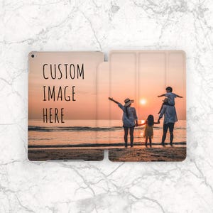 Może przedstawiać: Prostokątne etui na tablet z nadrukiem zdjęcia rodziny na plaży o zachodzie słońca. Lewy panel zawiera czarny napis CUSTOM IMAGE HERE, a prawy panel przedstawia sylwetki trzech osób na tle zachodzącego słońca.