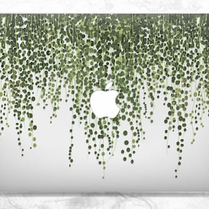 May include: A white laptop computer with a green and white design of hanging vines. The Apple logo is visible on the back of the laptop.