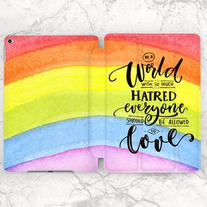 May include: A rainbow-colored tablet case with a watercolor design. The case features the text "In a world with so much hatred everyone should be allowed to love" in black script. The case is open and has a marble background.