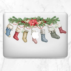 May include: A silver laptop with a Christmas-themed sticker featuring a garland of greenery, red berries, and a poinsettia with six stockings hanging from it. The stockings are red, blue, green, and white with a variety of patterns.