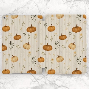 Pode incluir: Uma capa de tablet bege com um padrão repetido de abóboras, folhas e pequenas flores amarelas. As abóboras são em tons de laranja e bege, sobre listras verticais bege.