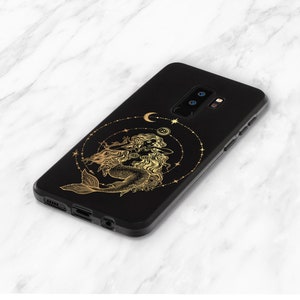 May include: Black phone case with a gold design of a mermaid with a crescent moon and stars.