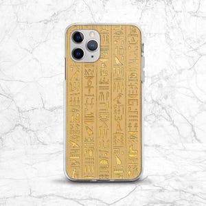 May include: A clear phone case with a gold design of Egyptian hieroglyphics. The case is designed for an iPhone.