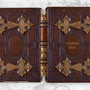 Pode incluir: Uma capa de iPad de couro marrom com um design em relevo dourado. A capa está fechada e tem uma lombada com detalhes dourados. A capa frontal tem o texto "CUSTOM TEXT" em letras douradas.