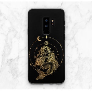 May include: Black phone case with a gold mermaid design. The mermaid is surrounded by a circle of stars and moons.