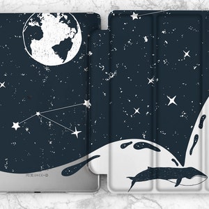 May include: A dark blue iPad case with a white whale jumping out of the water, a constellation of stars, and a white globe. The case has a distressed, vintage look.