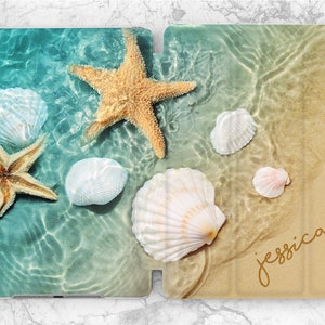 Può includere: Una custodia per iPad a tema spiaggia con uno sfondo di acqua blu e verde, una stella marina e conchiglie. La custodia ha il nome "jessica" scritto in oro nell'angolo in basso a destra.