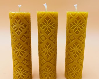 May include: Three yellow beeswax candles with a snowflake pattern. The candles are arranged in a row on a light orange surface.