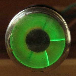 May include: A close-up of a green glass tube with a black centre. The tube is lit up and glowing green.