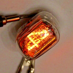 Peut inclure: Tube Nixie orange et jaune vif dans un boîtier en verre transparent. La structure interne est en forme de grille. Monté sur une base métallique. La source de lumière est orange vif.