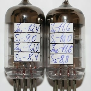 May include: Two vintage glass vacuum tubes with silver-coloured metal caps. Each tube has a white label with handwritten blue text indicating measurements: "Iz-12.4, S-9.0, Iz-12.0, S-8.4" and "Iz-11.6, S-10.0, Iz-11.6, S-8.8".