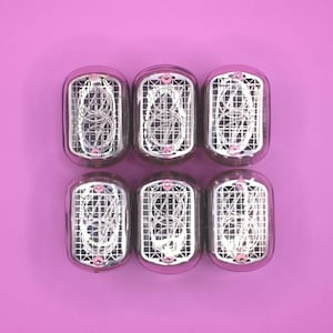 Puede incluir: Seis tubos Nixie vintage dispuestos en dos filas de tres, cada uno encerrado en un tubo de vidrio transparente. Los tubos muestran el número ocho con una rejilla de alambre y un acento rosa. El fondo es de color lila claro.