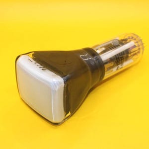 May include: A vintage cathode ray tube (CRT) with a rectangular screen and a clear glass tube. The screen is white, and the tube is encased in black material. The CRT is set against a yellow background.