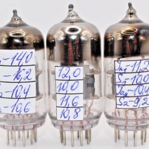 May include: Three glass vacuum tubes with silver tops and handwritten labels. The labels include measurements in millimetres and the text "J-14,0", "S-100", "Ja-104", "S2-106", "12,0", "10,0", "11,6", "10,8", "J-11,2", "S-100", "Ja-104", "S2-9,2".