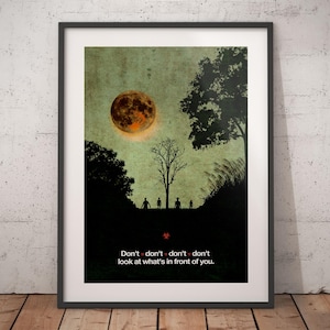 May include: Framed art print depicting a surreal scene with a large, orange moon in a green sky. Silhouetted trees and figures are in the foreground. The text "Don't...don't...don't look at what's in front of you" is at the bottom.