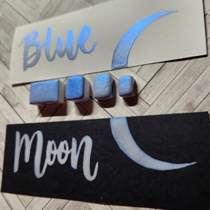 May include: Blue and white paint with the words "Blue Moon" written in white on a black background. There are four small blue paint squares.