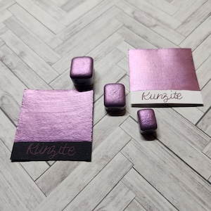 Pode incluir: Quatro pequenas bandejas de tinta roxa metálica com a palavra "Kunzite" escrita em duas das bandejas.