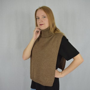 Puede incluir: Un chaleco de punto marrón de cuello alto. El chaleco es sin mangas y tiene un corte holgado.