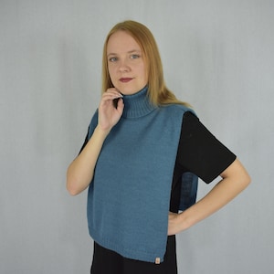 Könnte beinhalten: Ein blauer Strick-Rollkragen-Einsatz mit geripptem Kragen und ärmellosem Design, das Brust und Rücken bedeckt. Das Kleidungsstück ist in feiner Strickoptik gefertigt und verfügt über ein kleines rechteckiges Etikett am unteren Saum.