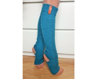 May include: A pair of teal knit leg warmers featuring a ribbed cuff at the top and a heel opening at the bottom. A small rectangular brown leather tag with the text Hand Made is attached to the upper ribbed section of the right leg warmer.
