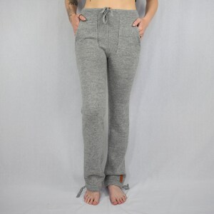 Puede incluir: Pantalones de punto en gris jaspeado con dise&ntilde;o de cintura alta con cord&oacute;n, dos bolsillos delanteros y cordones ajustables en el bajo de cada pierna. Una peque&ntilde;a etiqueta rectangular marr&oacute;n es visible en la pierna izquierda.