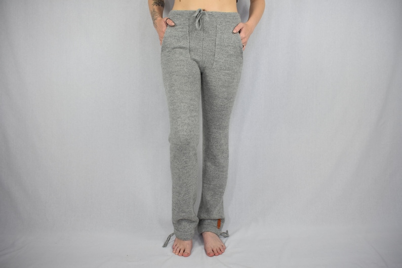 Puede incluir: Pantalones de punto en gris jaspeado con dise&ntilde;o de cintura alta con cord&oacute;n, dos bolsillos delanteros y cordones ajustables en el bajo de cada pierna. Una peque&ntilde;a etiqueta rectangular marr&oacute;n es visible en la pierna izquierda.