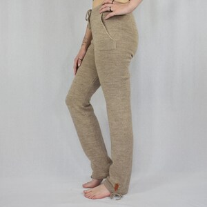 Puede incluir: Pantalones de punto beige con cintura de cord&oacute;n, bolsillos laterales y una peque&ntilde;a etiqueta rectangular marr&oacute;n cerca del dobladillo. Los pantalones tienen una silueta de pierna recta con lazos ajustables en la parte inferior de cada pierna.
