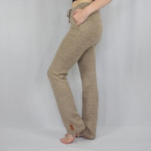 Puede incluir: Pantalones de punto beige con cintura de cord&oacute;n, bolsillos laterales y una peque&ntilde;a etiqueta rectangular marr&oacute;n cerca del dobladillo. Los pantalones tienen una silueta de pierna recta con un detalle de lazo en la parte inferior de tela texturizada.