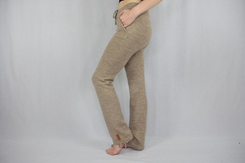 Puede incluir: Pantalones de punto beige con cintura de cord&oacute;n, bolsillos laterales y una peque&ntilde;a etiqueta rectangular marr&oacute;n cerca del dobladillo. Los pantalones tienen una silueta de pierna recta con un detalle de lazo en la parte inferior de tela texturizada.