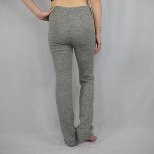 Puede incluir: Un pantal&oacute;n de punto gris jaspeado con dise&ntilde;o de cintura alta y una costura vertical visible en la parte central trasera. El pantal&oacute;n tiene una silueta ajustada que llega hasta los tobillos, confeccionado en un tejido con textura.